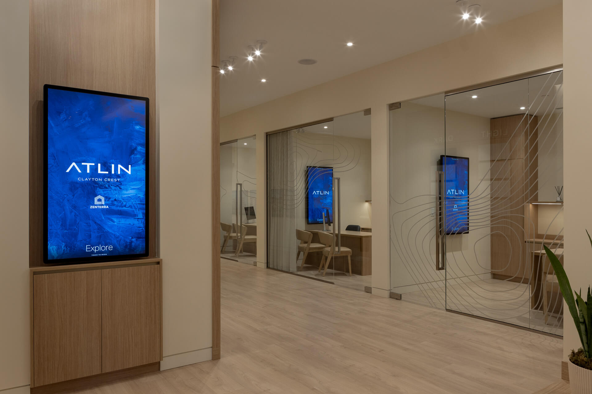 Bright interior corridor of the Zenterra Atlin sales center, displaying a digital interactive touchscreen kiosk and private glass-walled consultation rooms etched with topographical design patterns