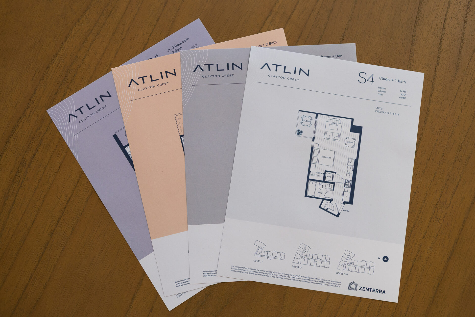 A fan layout of official Zenterra printed marketing brochures and floor plan pamphlets for Atlin Clayton Crest on a dark wood table, detailing a Studio plus 1 Bath S4 layout configuration