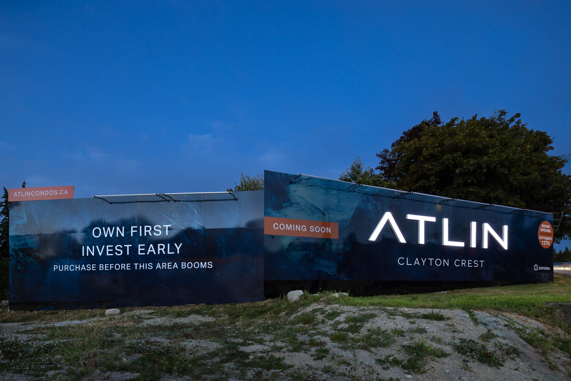 Large illuminated outdoor real estate billboard at dusk for Atlin Clayton Crest condos by Zenterra, featuring the text Own First Invest Early Purchase Before This Area Booms against a deep blue evening sky
