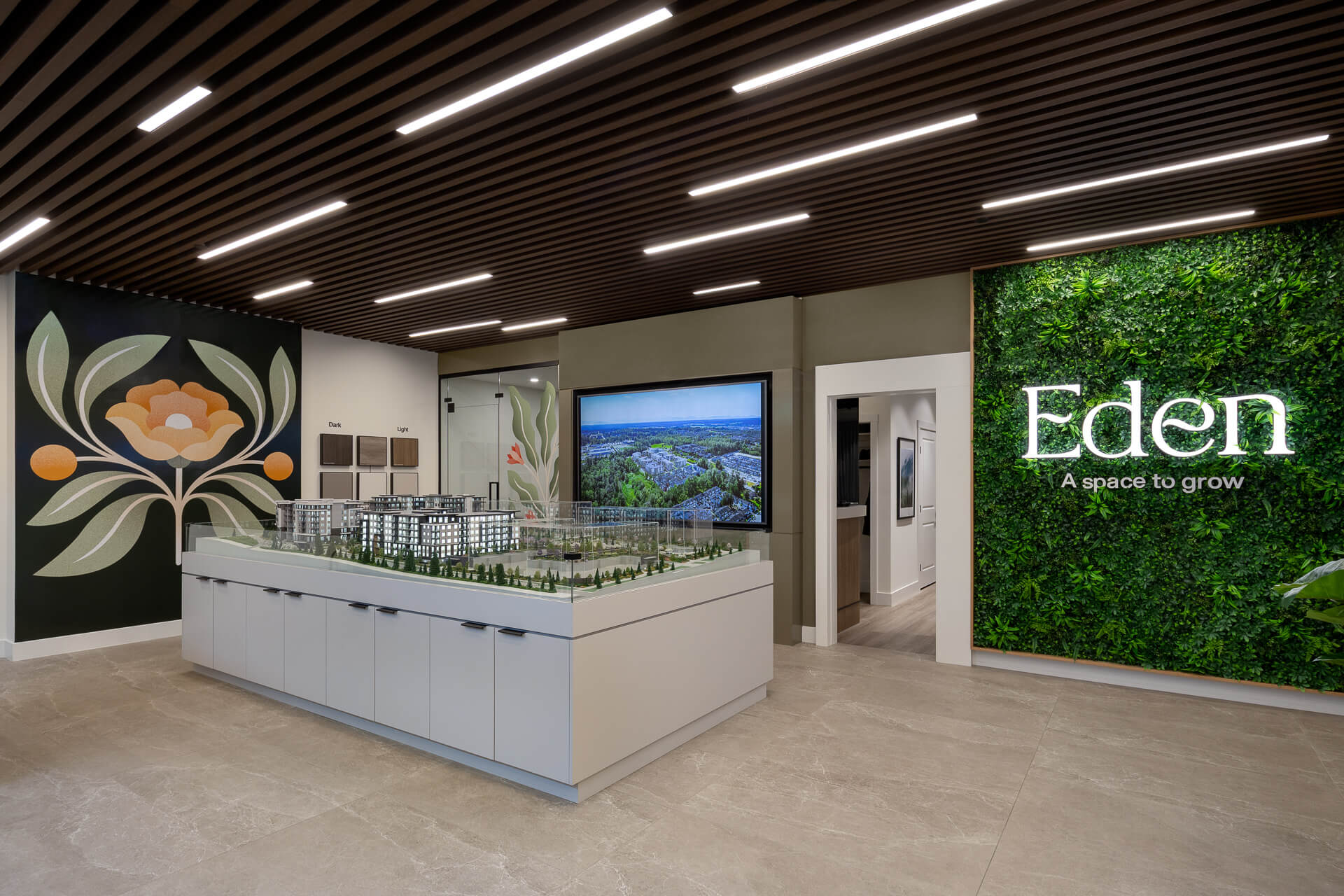 Bright presentation center interior for Eden condos by Zenterra, featuring an architectural community scale model, slatted wood ceiling with recessed LED strip lights, and a vibrant green moss feature wall with illuminated text reading Eden A space to grow