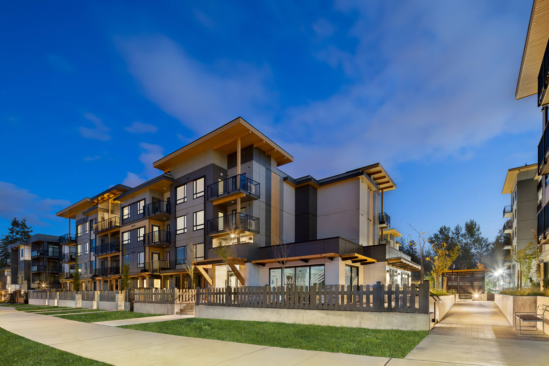Angled dusk architectural photograph of the Eden residential condo complex, highlighting ground-floor patios with fencing, landscaped walkways, and a bright blue evening sky