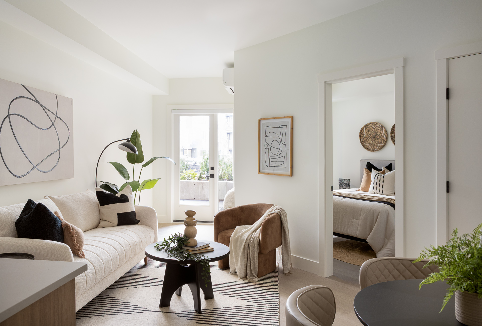 Modern bright living room interior at The Commons by Zenterra, displaying an open floor plan with a white sofa, minimalist decor, and view into the bedroom