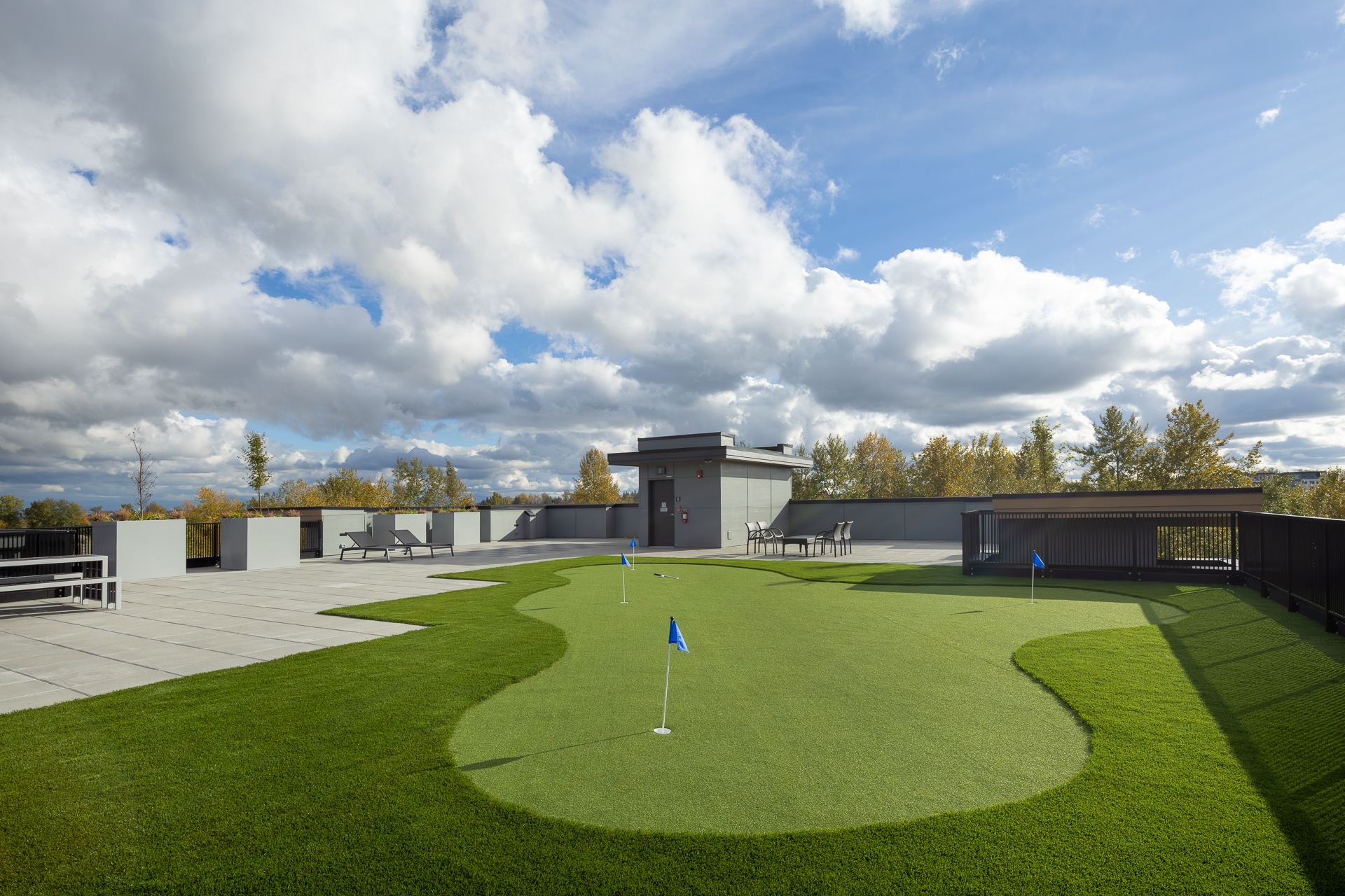 The Commons 5000 square foot rooftop terrace amenity featuring an artificial turf putting green with blue flags under a bright blue cloudy sky
